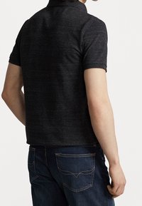 Short-sleeve polo shirt in dark gray fabric, featuring a collar and a fitted design, paired with dark blue jeans with visible back pockets.