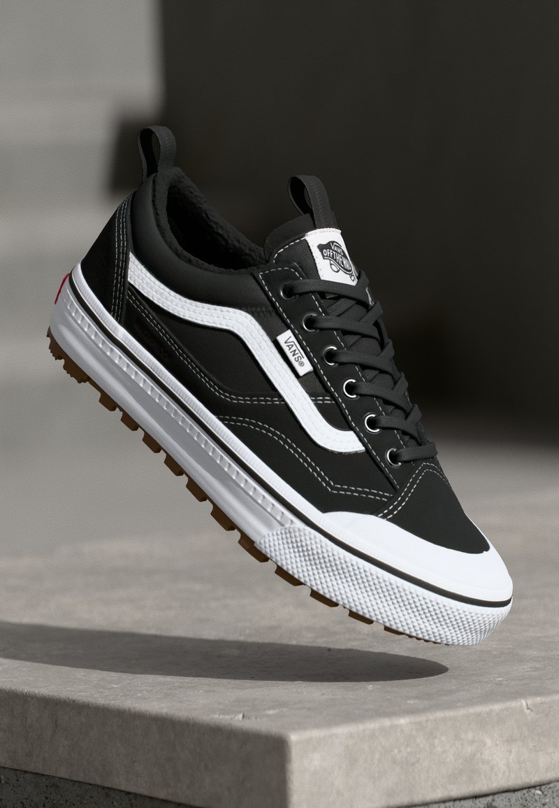 Black and white sneaker featuring a leather and textile upper, rubber outsole, lacing system, and a logo patch on the tongue.