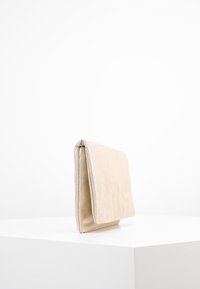 Béžové psaníčko s texturovaným povrchem, štíhlým obdélníkovým tvarem a skládacím designem. Hrany mají jemný kovový lesk.