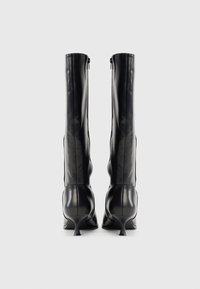 Μαύρες μπότες μέχρι το γόνατο από λείο δέρμα, με λεπτό τακούνι και φερμουάρ στο πίσω μέρος. Κομψή, εφαρμοστή σιλουέτα.