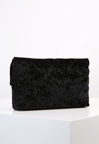 Černá sametová kabelka v kombinaci s měkkou texturou, obdélníkovým tvarem a designem s složeným klopou. Minimalistická a elegantní, bez viditelného kování.