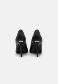 Escarpins noirs en cuir avec un bout pointu, au design élégant et à talon aiguille étroit. Présente une petite plaque logo sur le talon.