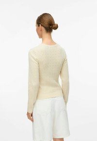 Lichtbeige geribde trui met lange mouwen en een ronde hals, met subtiele textuurdetails. Gecombineerd met witte shorts, zonder zichtbare hardware.