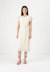 Robe en dentelle crème avec des manches courtes à volants et une taille nouée, dotée d'un ourlet au niveau du genou et d'une texture à motifs intriqués.