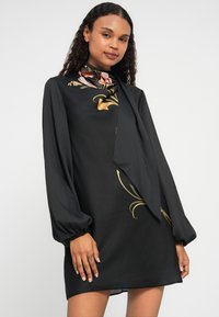 Rochie neagră cu mâneci lungi, model floral în nuanțe de roz și aur, detaliu cu funda la gât, material ușor cu textură, croială lejeră.