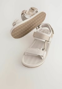 Leichte Sandalen in Beige und Weiß. Sie verfügen über verstellbare Riemen, eine strukturierte Sohle mit Zickzackmuster und ein offenes Design für Atmungsaktivität.