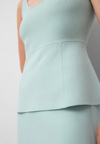 Miętowo-zielony dzianinowy top z okrągłym dekoltem i baskinką. Tkanina ma prążkowaną teksturę, podkreślającą kształt i wzór.