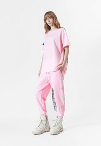Camiseta rosa oversized con un parche en el frente; pantalones de chándal rosas a juego con bordado lateral. Modelo llevando botas de combate de color claro.