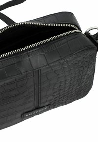Sac bandoulière en cuir noir avec un motif crocodile texturé, fermeture éclair argentée et bandoulière réglable. Comprend une étiquette de marque à l'avant.