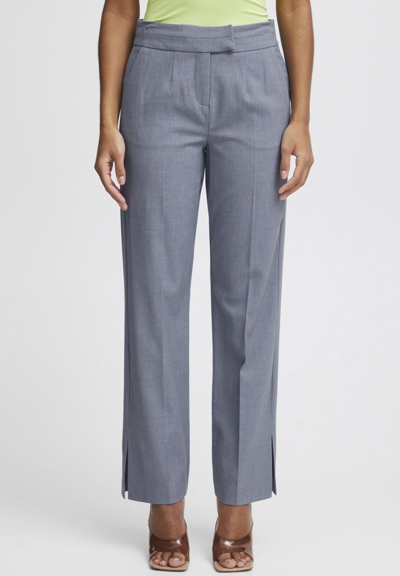 Pantalons habillés gris avec une taille haute, des plis, des fentes latérales à l'ourlet et une texture lisse. Assortis à des talons bruns à bouts ouverts.