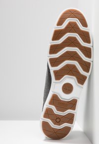 Šedá a černá podrážka tenisky s bílým mezipodešví a hnědým gumovým vzorem pro trakci. Obsahuje branding "SENSORFLEX" a logo.