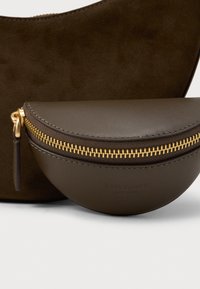 Bolsa de camurça castanha com uma bolsa menor de couro verde-oliva, apresentando um zíper dourado e uma alça de couro na frente.
