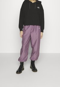 Felpa nera con un motivo testurizzato e logo, abbinata a pantaloni jogger larghi di un leggero viola e stivaletti neri con lacci.