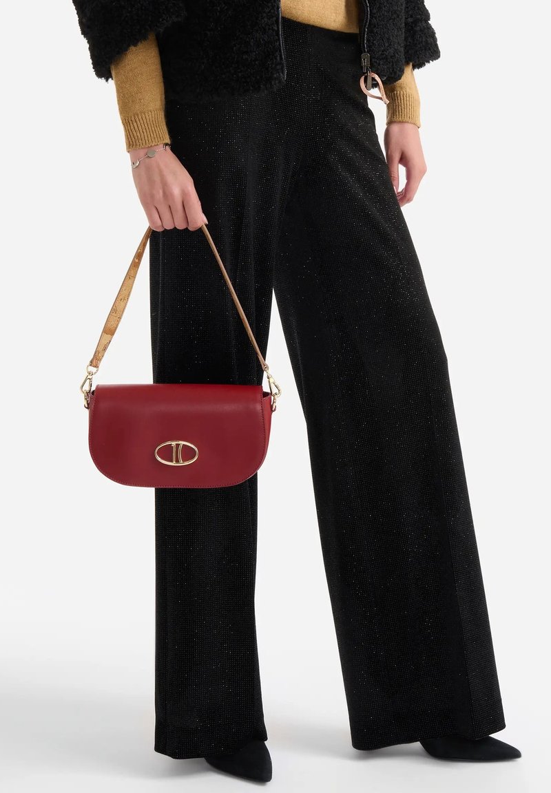 Borsa a mano in pelle rossa con chiusura in metallo dorato, abbinata a pantaloni neri larghi con sottili scintillii e a una giacca nera con texture.