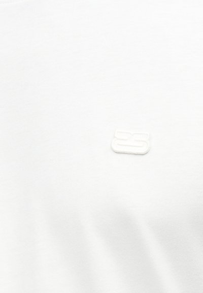 Άσπρο ύφασμα με ένα μικρό, ανάγλυφο λευκό λογότυπο που αποτελείται από δύο οριζόντιες ράβδους στοιχισμένες η μία πάνω στην άλλη.