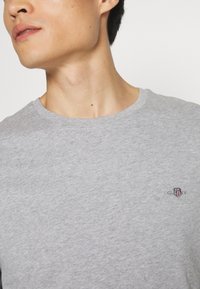 Grijze katoenen t-shirt met een ronde halslijn en korte mouwen. Heeft een klein geborduurd logo op de borst. Soepele textuur.