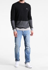 Svart och grå långärmad tröja med rund halsringning, kombinerad med ljusblå jeans och vita sneakers. Tröjan har en färgblockeringsdesign.