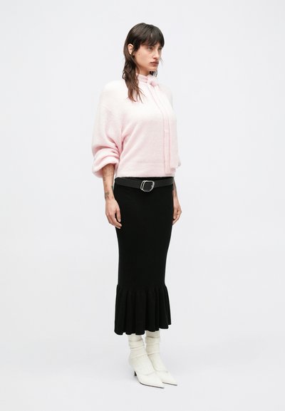 Svetloružový pletený sveter s vysokým golierom, skombinovaný s čiernou rebrovanou sukňou s rozšíreným lemom. Štylizované s bielymi špicatými čižmami.