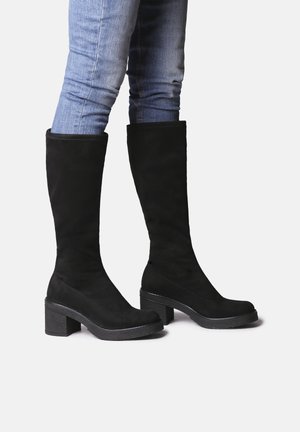 Botas de ante negras hasta la rodilla con tacones de bloque. Textura suave, punta redondeada y diseño minimalista. Adecuadas para diversos outfits.