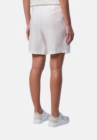 Pantaloni corti bianchi in lino con un taglio comodo e una cintura elastica. Tessuto liscia e lunghezza fino al ginocchio, abbinati a sneaker dai colori chiari.