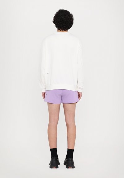 Hvid sweatshirt med lange ærmer, båret over lilla shorts, parret med sorte sko. Simple design, ingen synlige mønstre eller accenter.