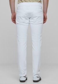 Pantalones de denim blanco mostrados desde atrás, con un diseño ajustado, dos bolsillos traseros y detalles de costura sutiles.