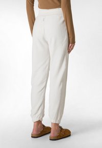 Fleece-Jogginghosen in Off-White mit elastischem Bund und Bündchen. Glatte Textur, minimalistisches Design, kombiniert mit braunen Slippern.