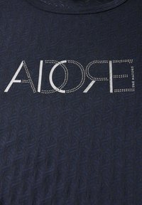 Námořnické tričko s texturovaným vzorem, na kterém je slovo "AIDORE" v stříbrných cvočcích a "THE NATURE" vytištěné bíle pod ním. Kulatý výstřih.