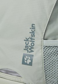 Hellgrauer Rucksack aus strukturiertem Stoff mit einem Logo und einem Pfotenabdruck an der Seite. Verfügt über eine Netzinnentasche für zusätzlichen Stauraum.