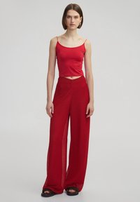 Top rosso senza maniche e pantaloni rossi a gamba larga. Il top è liscio e aderente; i pantaloni hanno una trama strutturata, una vestibilità ampia e una silhouette larga.