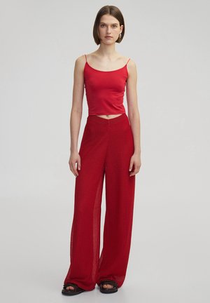Top rojo sin mangas y pantalones rojos de pierna ancha. El top es liso y ajustado; los pantalones tienen un tejido texturizado, suelto y una silueta amplia.