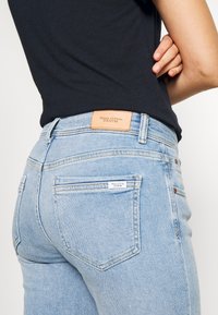 Světle modré džíny z denimu s hnědým koženým logem, designem s pěti kapsami a decentními švy. Texturovaná tkanina s ležérním střihem.