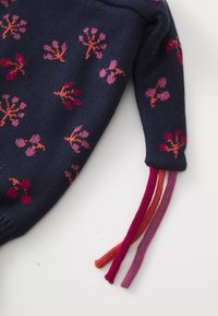 Gebreide trui met een marineblauwe achtergrond en bloemenpatronen in roze en rood. Verzien van meerkleurige gevlochten franjes aan de mouwen.