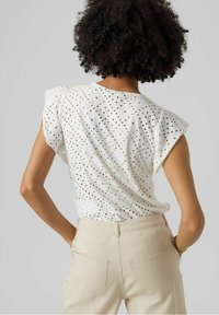 Top bianco a maniche corte con fori a occhio, caratterizzato da una vestibilità ampia e un motivo testurizzato. Abbinato a pantaloni beige a vita alta.