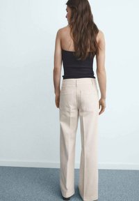 Beige wide-leg pants made of cotton, featuring two back pockets, paired with a black fitted top. The model is viewed from behind.