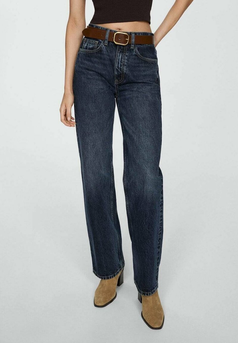 Jeans de pierna recta azul oscuro con un cinturón marrón, que cuentan con cinco bolsillos y detalles de costura sutiles. Modelo combinado con botas de tacón color beige.