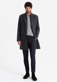Abrigo de lana gris oscuro con cuello de muesca, botones de un solo lado y un acabado texturizado. Combinado con un suéter gris claro y pantalones azul marino.