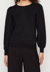 Maglione nero a maglia con maniche lunghe a sbuffo e polsini a costine. Presenta uno scollo rotondo e una silhouette aderente. Texture morbida.