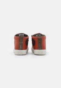 Czerwone skórzane trampki typu high-top z beżowym zamszowym paskiem z tyłu, białą gumową podeszwą oraz czarnym okrągłym logo na każdym pięcie.