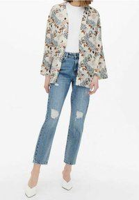 Giacca kimono a fiori in crema, con fiori blu e marroni, abbinata a jeans chiari strappati e décolleté bianchi a punta.