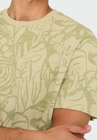 Camiseta de manga corta verde claro con un sutil patrón floral, textura suave y escote redondo. La tela parece suave y ligera.