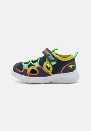 Baskets de sport bleu marine avec des accents vert lime et orange, dotées d'un design en maille, d'une sangle ajustable et d'une semelle blanche texturée.