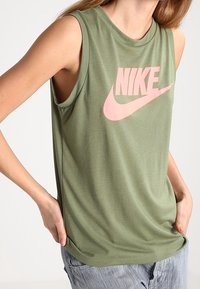 Grön ärmlös t-shirt i mjukt material, med en stor rosa Nike-logotyp över bröstet. Rund halsringning, avslappnad passform.