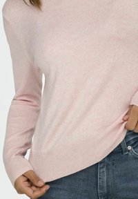 Pull en tricot rose clair avec un ourlet et des poignets côtelés, doté de manches longues et d'une coupe légèrement décontractée. Associé à un jean en denim bleu.