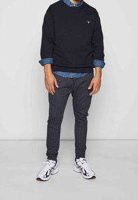 Czarna bluzka z okrągłym dekoltem noszona na dżinsowej koszuli, w połączeniu z spodniami w paski. Białe buty sportowe. Prosta, casualowa stylizacja.