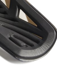 Suola in gomma nera, caratterizzata da un design intricato con scanalature e texture; un bordo liscio con sottili accenti metallici.