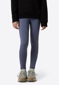 Leggings i dempet blått stoff, tettsittende design, glatt tekstur. Brukes med en svart oversized genser og grå treningssko.