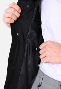 Giacca nera con una fodera interna liscia. Presenta chiusure a scatto e un piccolo anello per una chiusura sicura. Ideale per il layering.