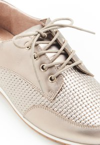 Sneaker in metallo chiaro con texture intrecciata sulla punta, lacci tondi, occhielli metallici e soletta imbottita. Il colore è champagne.