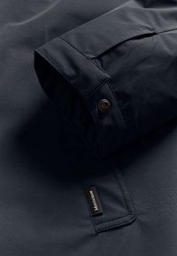 Artimųjų planas naktinės mėlynos striukės rankovės su snap mygtuko manžete ir mažu juodu audinio ženklu, pažymėtu "Matinique".